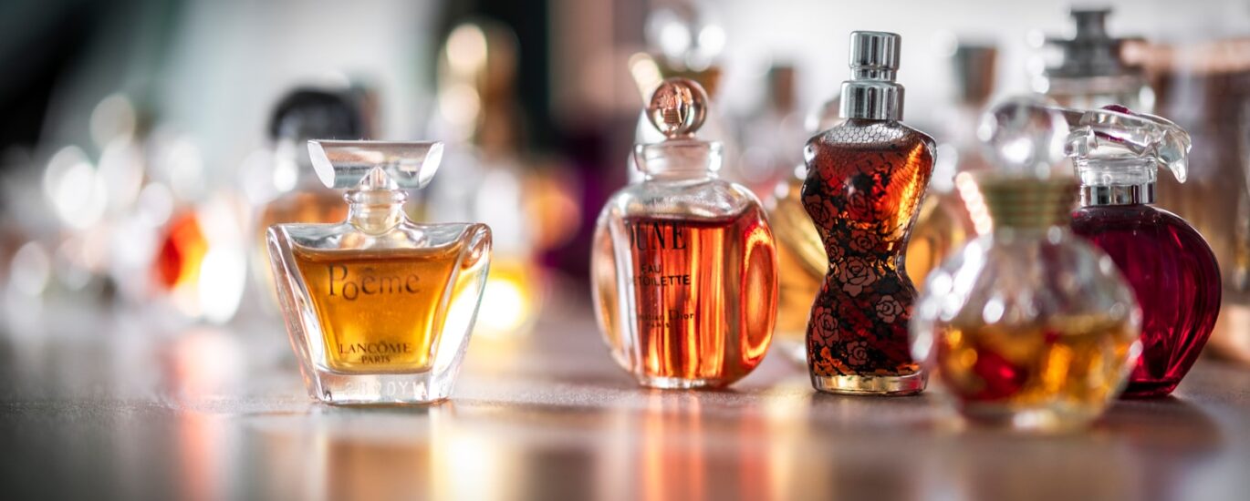 Collection of eco-friendly perfume bottles made from recycled materials, displayed on a natural wooden surface with greenery in the background, representing sustainable fragrance trends of 2025."