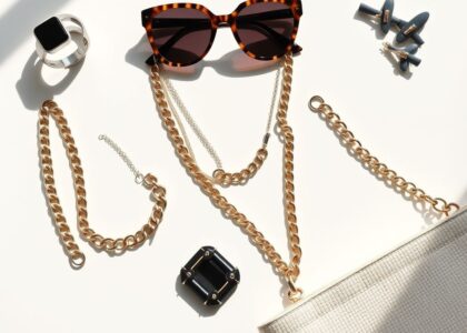 Flat lay of trending 2025 fashion accessories including a smart ring, oversized sunglasses, chunky chain necklaces, recycled handbag, and statement hair clips.
