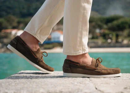 Stylish person wearing beige boat shoes and white pants walking on a boardwalk at sunset.
