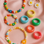 Close-up of colorful resin rings and beaded necklaces laid out on a pastel pink satin background, styled for a 2025 fashion flatlay.