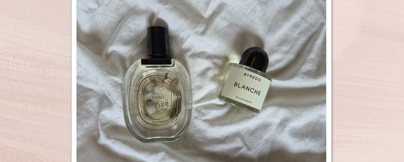 A bottle of clean, minimalistic perfume surrounded by soft white linen and summer light.