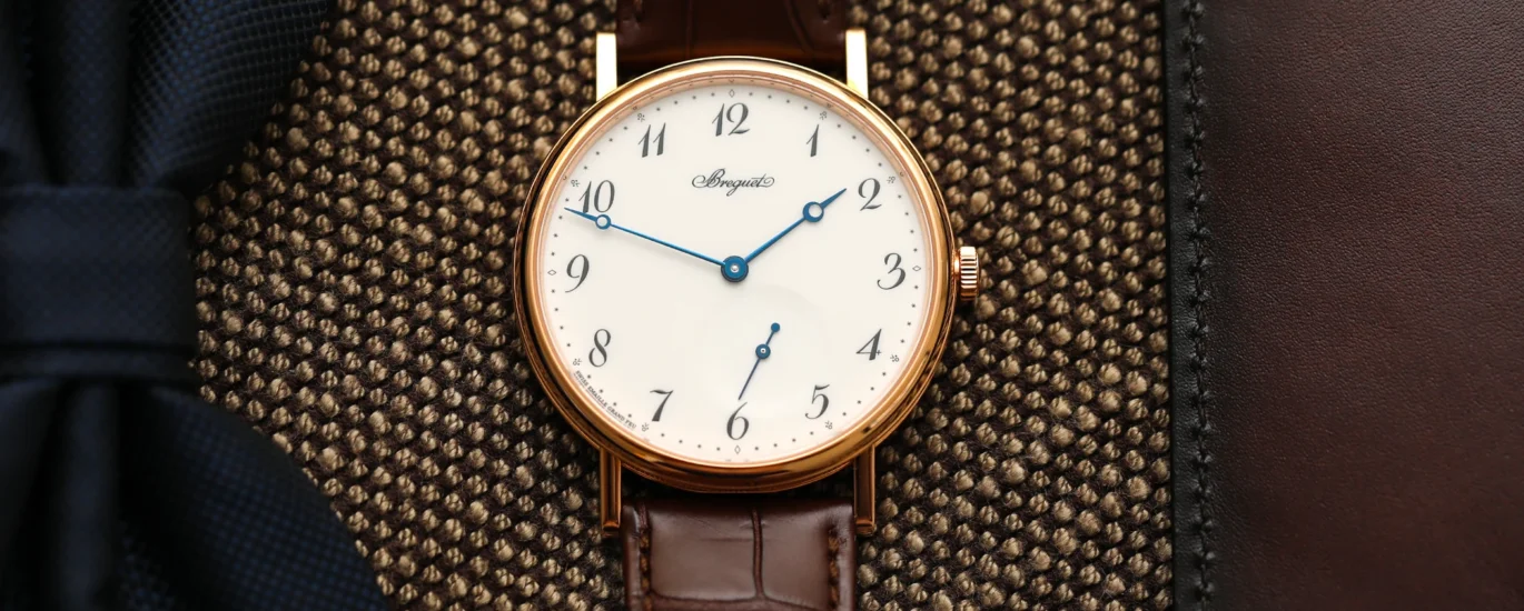 A neutral-toned flat lay featuring two vintage watches on a linen cloth with a leather journal and pen