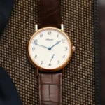 A neutral-toned flat lay featuring two vintage watches on a linen cloth with a leather journal and pen