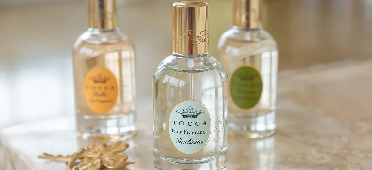 the Hair Perfume Trend by spraying a floral hair mist over styled waves in front of a vanity mirror, showcasing 2025 beauty routine