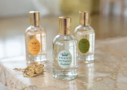the Hair Perfume Trend by spraying a floral hair mist over styled waves in front of a vanity mirror, showcasing 2025 beauty routine