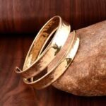 Gold metallic arm cuff paired with a colorful scarf-handle bag on a city rooftop, perfect for summer fashion 2025.