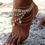 Woman showcasing anklet trend 2025 in layered gold and pearl anklets at the beach